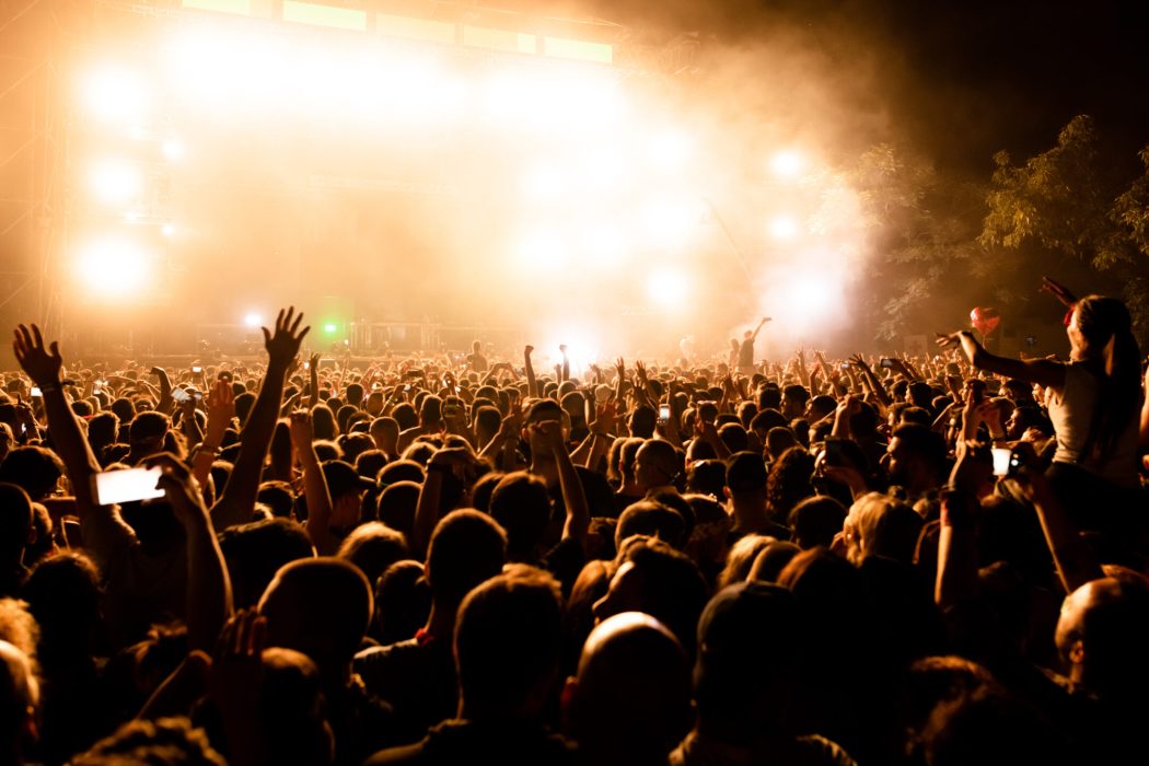 Rear view of large group of music fans in front of the stage during music concert by night. Copy space.